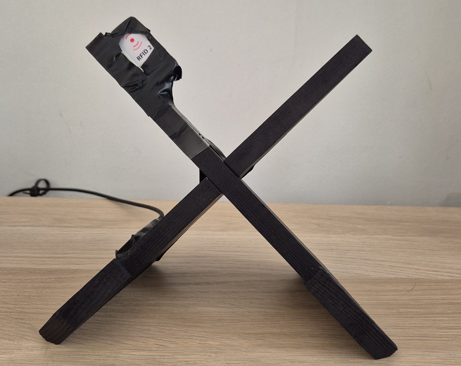 The empty record stand: two black wooden boards crossed in an X, with a small white RFID 2 module gaffer-taped to the top of one board and a cable running down to the taped-up ESP32 near the base