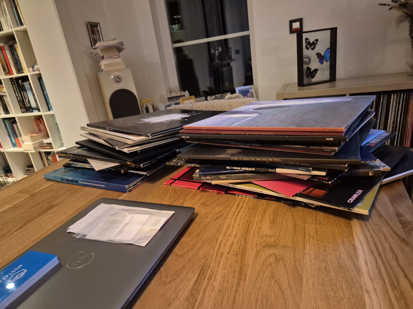 Two stacks of vinyl records on a wooden table, including The Mob's Let the Tribe Increase and IDLES live at Le Bataclan, next to a closed laptop with a small envelope of RFID stickers on it